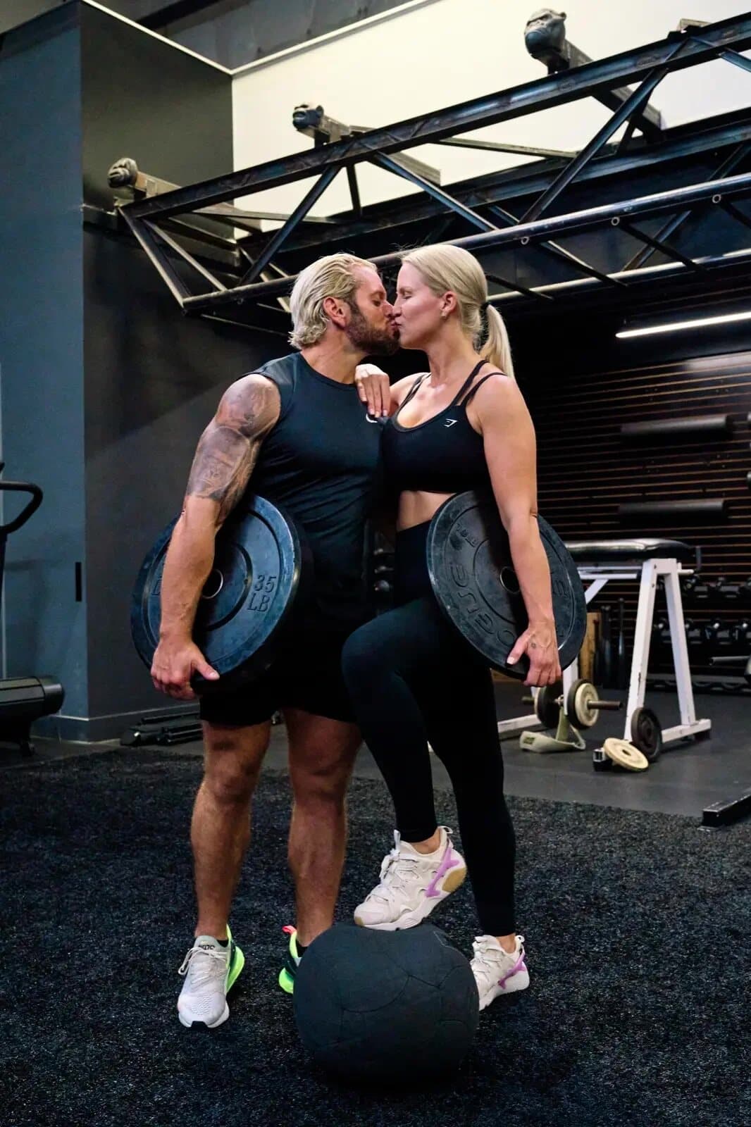 Jarred and Katelyn Curcio kissing while holding weight plates in the gym